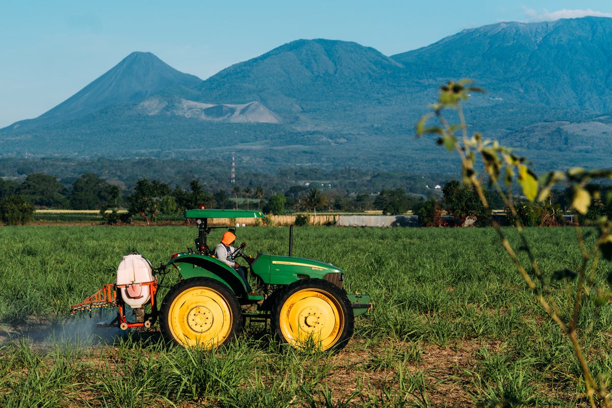 Trator realizando atividade agrícola em lavoura com montanhas ao fundo.