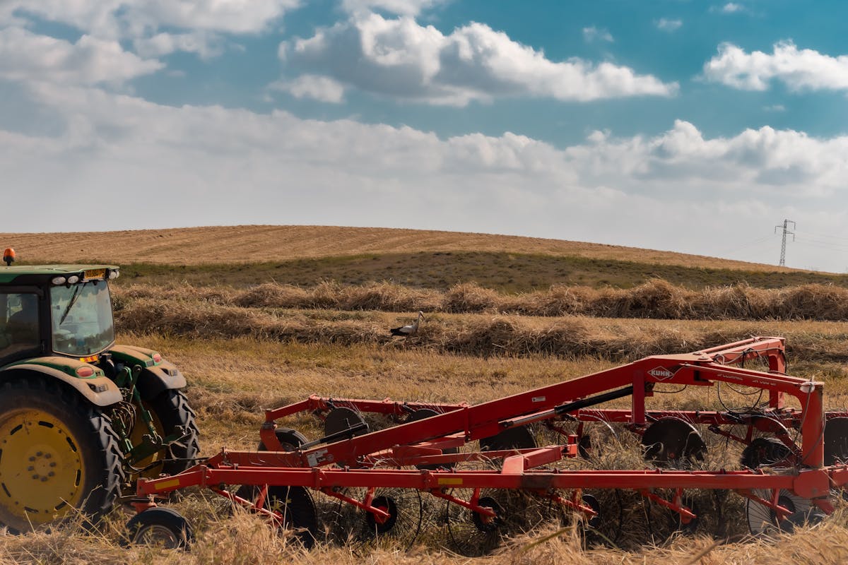 Trator com implementos agrícolas trabalhando em área de cultivo após a colheita.