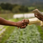 Duas pessoas apertando as mãos em propriedade rural durante negociação agrícola.