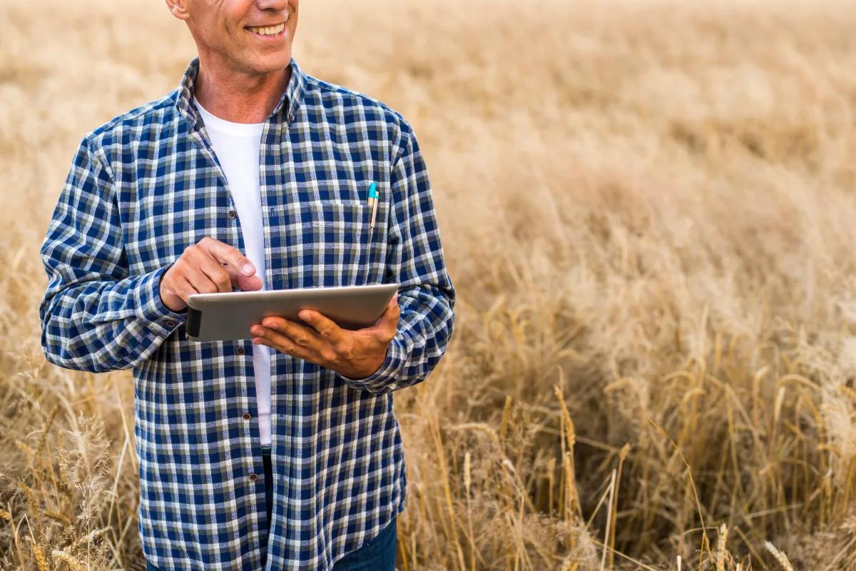 Produtor rural utiliza tablet em plantação para acompanhar dados climáticos que influenciam a produtividade agrícola.
