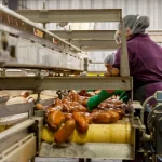 Funcionários atuando em linha automatizada de produção de embutidos em indústria alimentícia.