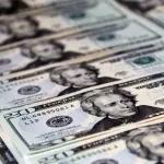 Várias notas americanas de vinte dólares dispostas de forma organizada e sequencial em fileiras paralelas sobrepostas, com foco nítido na cédula central e desfoque gradual ao fundo.