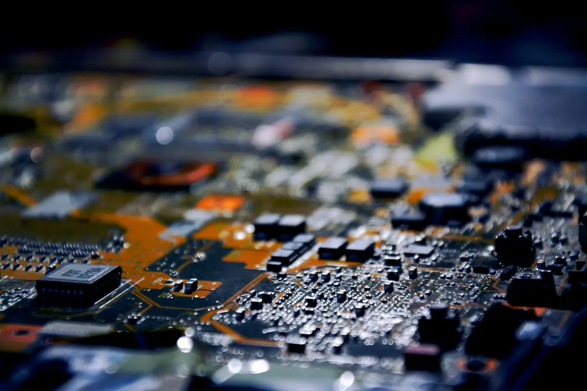 Macrofotografia de uma placa de circuito impresso com diversos componentes eletrônicos, microchips e soldas detalhadas, sob iluminação fria e com fundo desfocado.