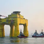 Grande plataforma conversora offshore amarela chamada DolWin epsilon sendo rebocada no mar por quatro rebocadores sob um céu claro.